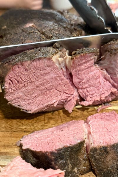 Knife slicing into a finished sous vide chuck roast on a cutting board, revealing a tender, evenly cooked pink interior and dark seasoned crust