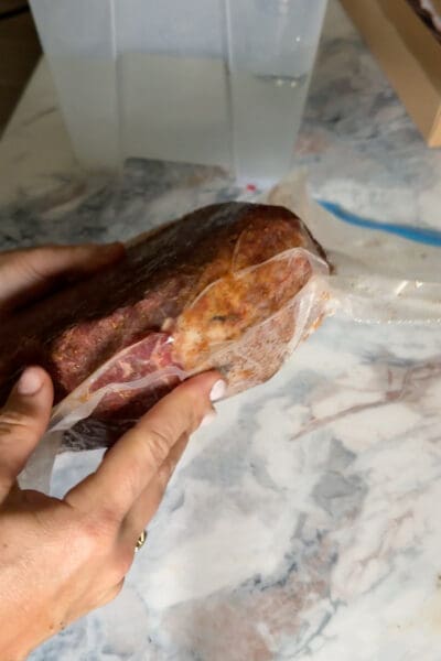 Hands holding a seasoned chuck roast vacuum-sealed tight in a bag with the air removed, ready to sous vide