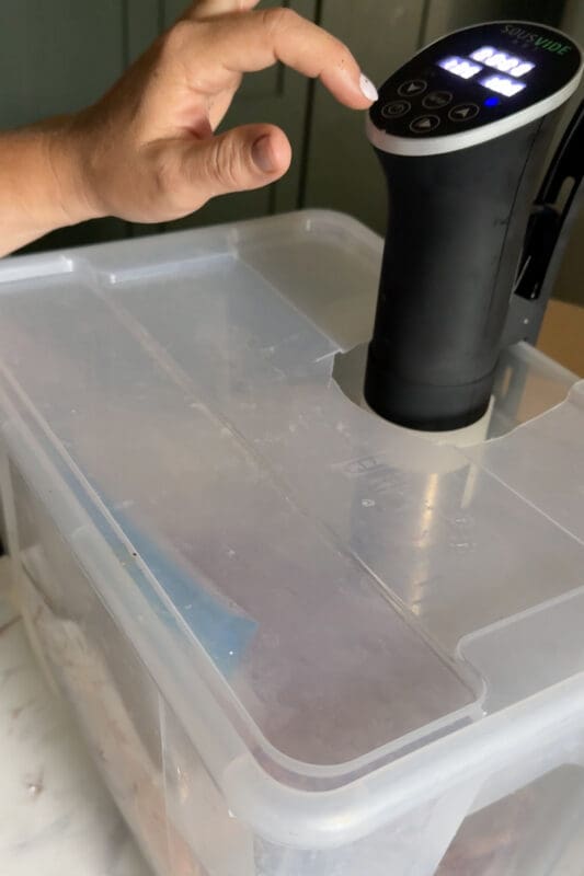 SousVide Art immersion circulator clipped into a plastic tote lid, being set at the touch controls