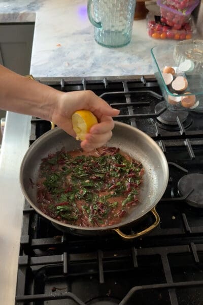 Crystel squeezing fresh lemon juice over the wilted beet greens in the pan to brighten the flavor before serving