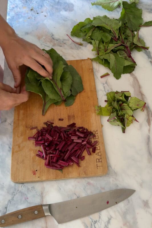 Crystel stacking and rolling beet green leaves on a cutting board next to a pile of chopped ruby stems