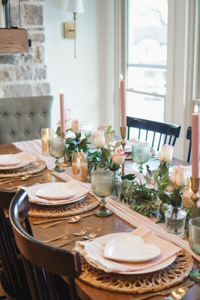 Valentine's table with a blush gauze runner, white heart-shaped plates layered on pink dinner plates, gold flatware, green ribbed goblets, and pink taper candles, one of my favorite seasonal tablescape ideas
