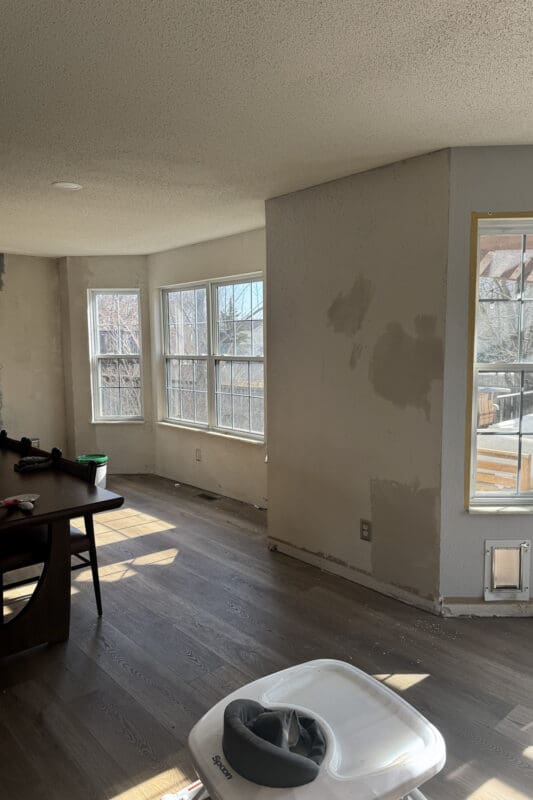 Empty bay window nook with three white windows, patched drywall, and dark wood look flooring before any trim or bench was added