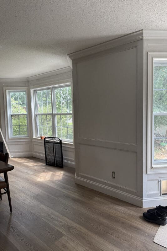 Bay window nook in a dining area with white crown molding and picture frame wall trim, sitting empty before the window bench build