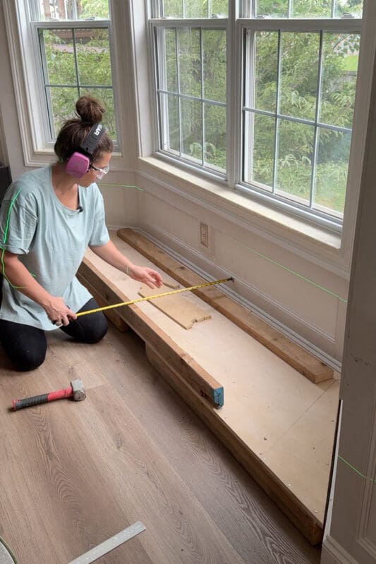 Crystel sitting on the plywood base using a pneumatic framing nailer to assemble the upper seat frame