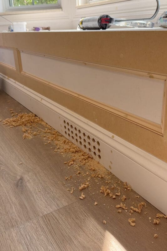 Close view of the finished hand drilled vent grid in the bench baseboard, letting air from the floor register flow out the front of the bench