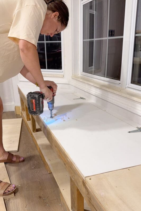 Crystel drilling a round finger hole near the front edge of the lift top panel to use as a handle for opening the bay window bench with storage