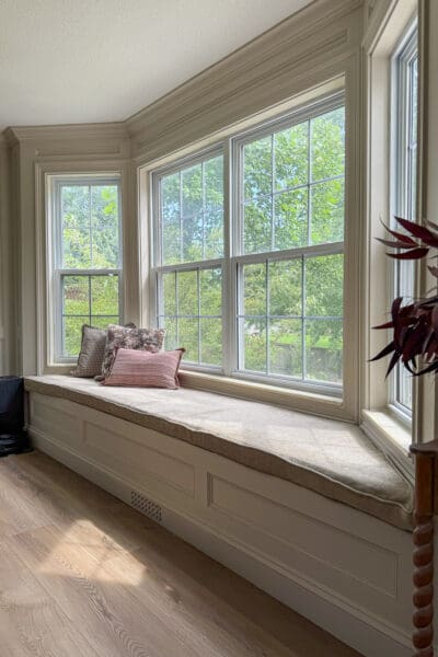 Wide view of the finished bay window bench with storage in a dining area, with the wall, trim, crown molding, and bench all painted the same warm beige