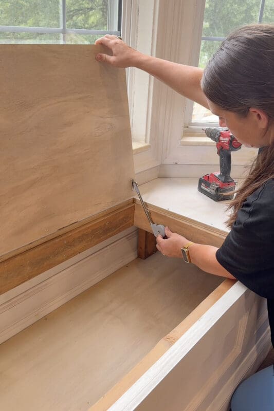 Crystel driving a screw to secure the lid support catch inside the bay window bench with storage so the top cannot fall shut