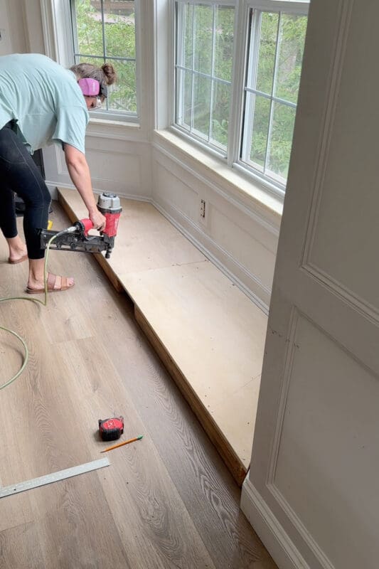 Crystel using a pneumatic framing nailer to fasten the plywood deck to the base frame of the bay window bench with storage