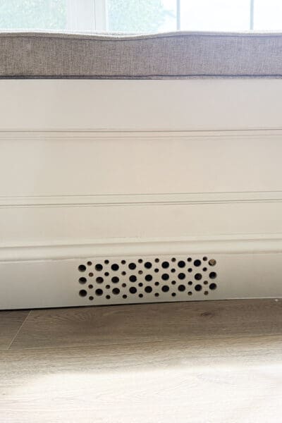 Close view of the hand drilled air vent in the painted bench baseboard, with the cushion edge above it