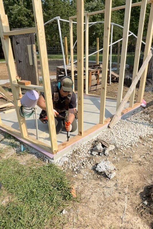Man using a single shot powder actuated nailer to drive a fastener through the bottom plate and anchor the wall framing to the concrete slab