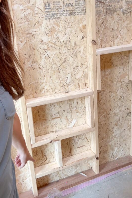 Woman pointing out the framed opening in the interior wall of a chicken coop where a small chicken door will lead out to the run