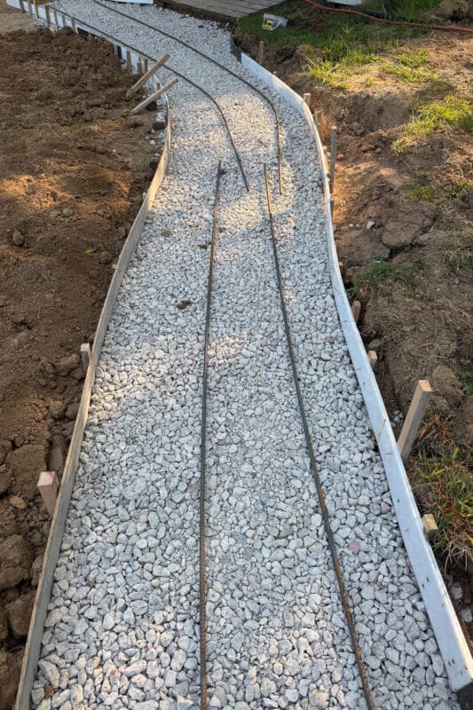 Two lengths of rebar running down the center of the gravel base inside the forms for the concrete path in the backyard, ready for the pour