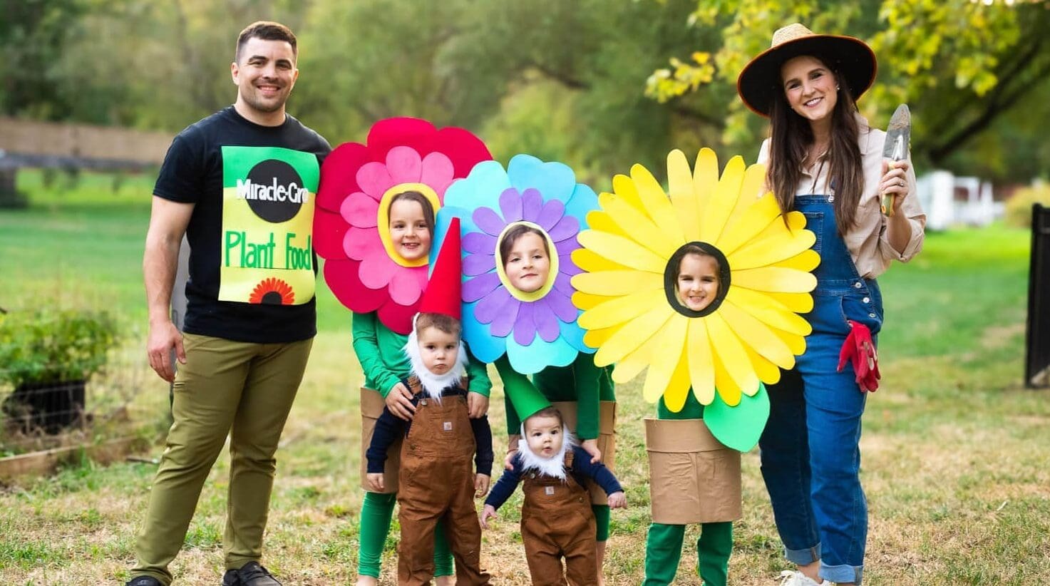 Garden-themed Halloween for big families: bright flower headpieces with pot skirts, toddler gnome hats and beards, dad in fertilizer T-shirt, and mom gardener in overalls.