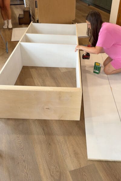 Crystel driving screws into the plywood joints of the assembled cabinet box to reinforce the brad nailed frame for the DIY fireplace built ins