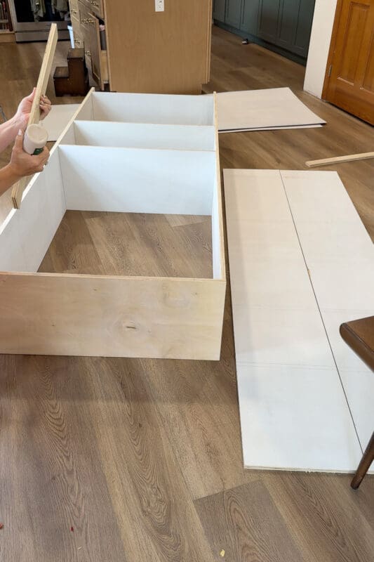 Crystel applying wood glue to a plywood brace before setting it across the top of the assembled cabinet box for the DIY fireplace built ins