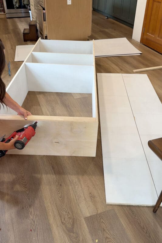 Crystel nailing the top brace into place on the plywood cabinet box, completing the frame for the DIY fireplace built ins