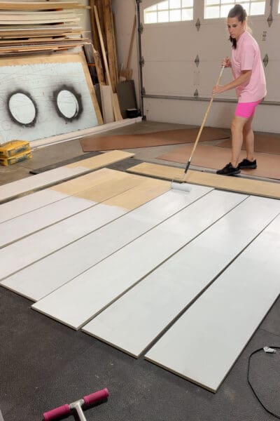 Crystel priming cut plywood panels with a roller on the garage floor before assembling DIY cabinets for her dining room.