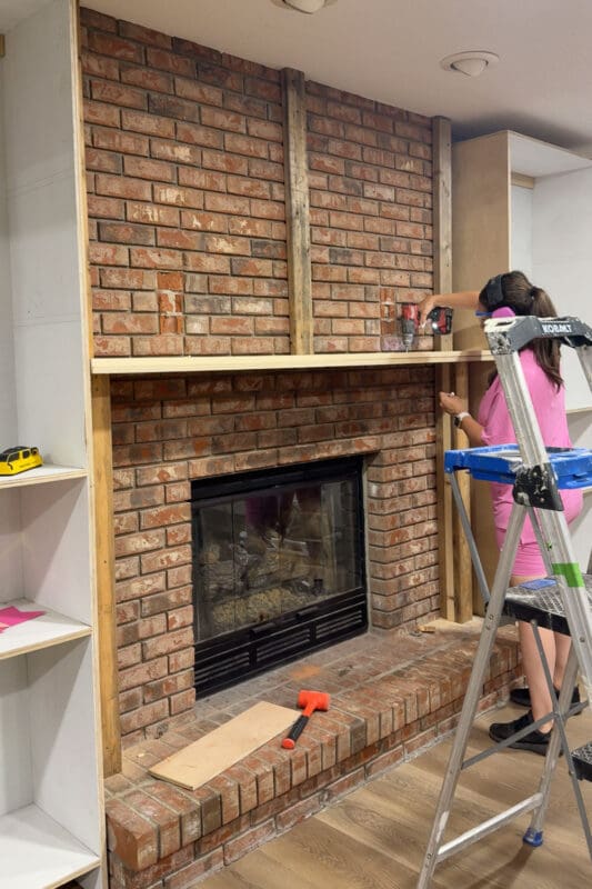 Crystel driving fasteners into the doubled mantel boards where they meet the 2x4 blocking on the DIY fireplace built ins