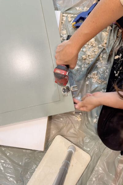Crystel screwing concealed hinges into the bored cup holes on a painted cabinet door for the DIY fireplace surround