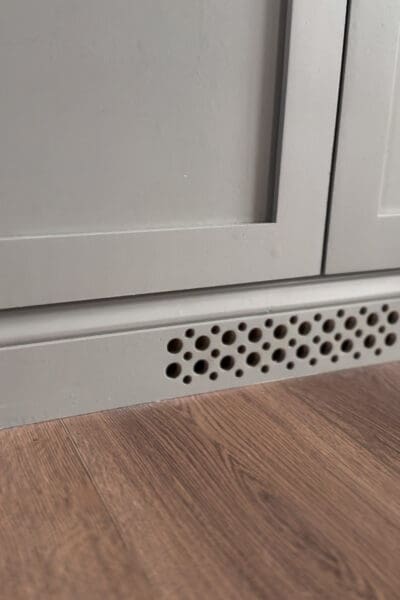 Close view of the drilled vent holes in the baseboard beneath the cabinet doors, allowing airflow for the electronics stored inside the DIY fireplace surround