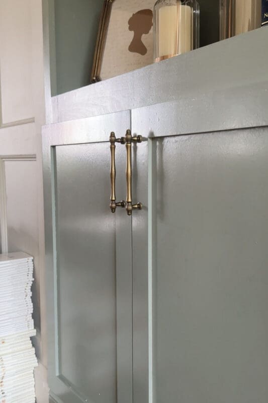 Close view of the aged brass pulls mounted on the sage green shaker doors of the DIY fireplace surround