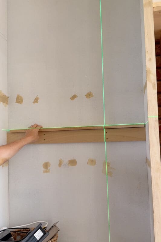 Holding a wood cleat along the laser line on the back wall of the cabinet to support the relocated shelf on DIY built-ins.