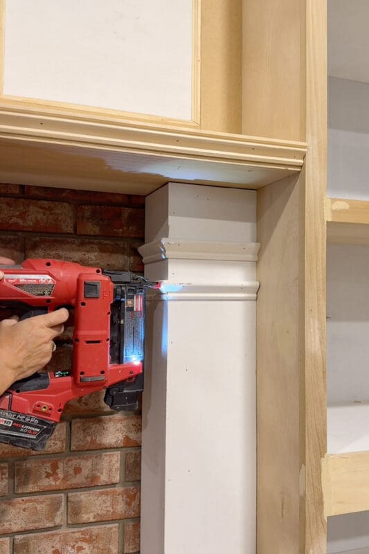 Close view of Crystel nailing profiled cap trim near the top of the plywood wrapped column, just under the mantel on the DIY fireplace surround