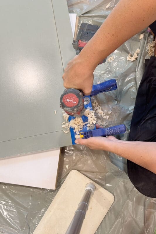 Crystel using a Kreg concealed hinge jig to bore a hinge cup hole into the edge of a painted shaker cabinet door for the DIY fireplace surround