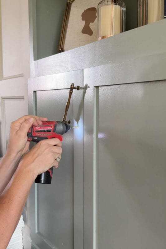 Crystel drilling a second hole to mount an antique brass pull onto the cabinet door of the DIY fireplace surround