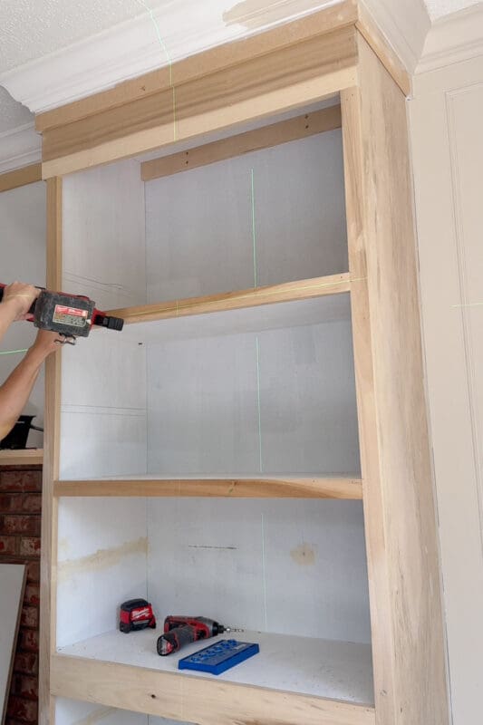 Crystel nailing trim onto the front edge of an upper shelf, with the crown molding and column trim visible above on the DIY fireplace surround
