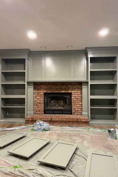 The DIY fireplace surround freshly painted sage green, with four shaker cabinet doors laid out on plastic sheeting to dry in the foreground