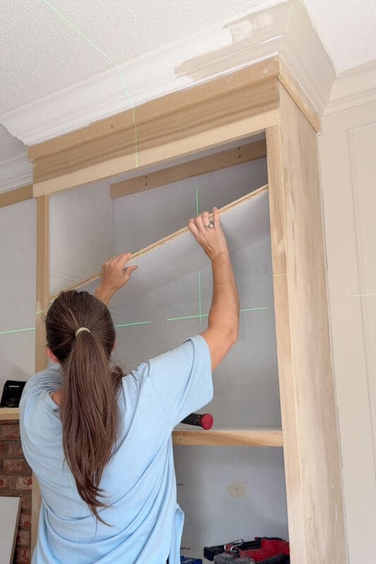 Crystel lowering an upper shelf onto the shelf pins inside the DIY fireplace surround cabinet