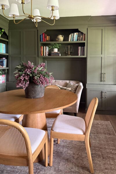 Back wall of the finished home library with an arched shelf opening above the loveseat, tall green cabinet doors with brass pulls, and panel molding running below the shelves.