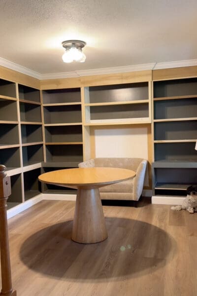 Home library built-in bookshelves after the build, with crown molding and baseboards installed but the shelf edges still raw wood and the walls unpainted, before the makeover started.