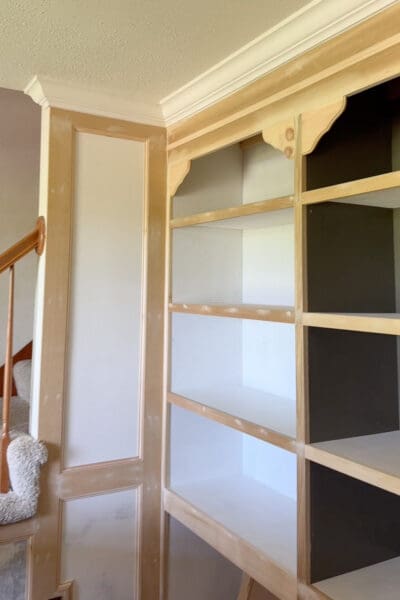 Corner of the home library built-in bookshelves with corbels installed, caulk and wood filler drying over the nail holes and seams, next to the box molding running along the adjoining wall.