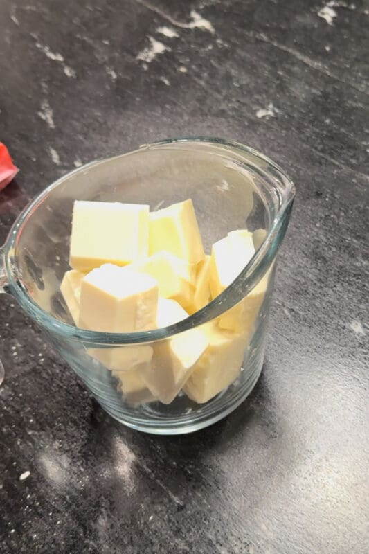 Squares of vanilla almond bark broken up in a glass measuring cup, ready to melt in the microwave for the second coating on fall treats.