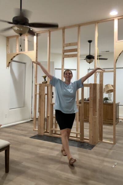 Crystel smiling with her arms stretched out in front of the room divider wall, with the arch framing installed in the walkway openings on both sides