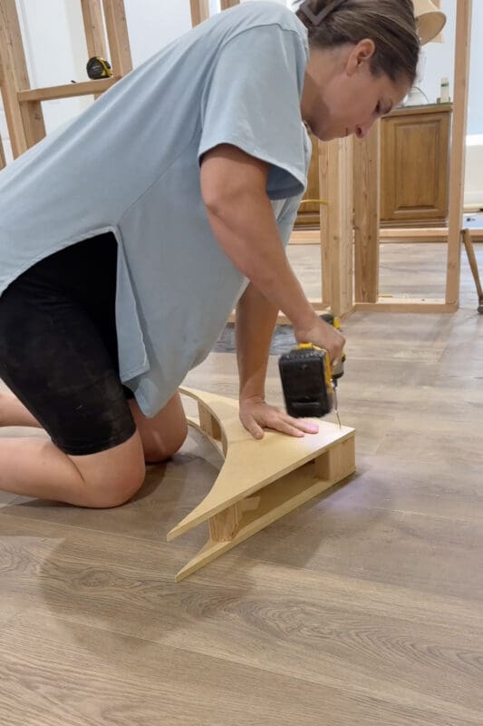 Crystel using an impact driver to screw a second curved arch piece onto the 2x4 blocks, sandwiching them together