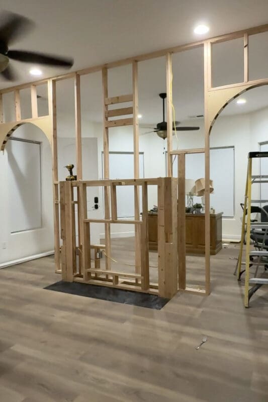 Framed room divider wall with a fireplace frame in the center and arch framing finished in the walkway openings on both sides