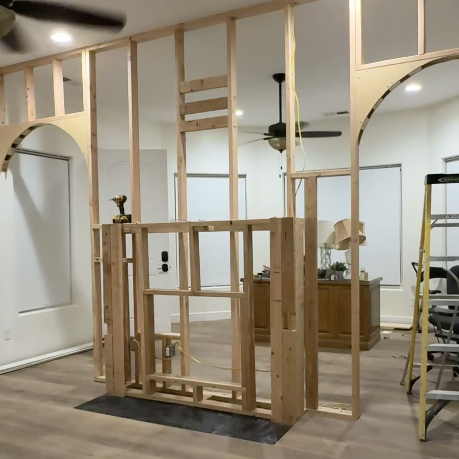 DIY arched doorway framing on both sides of a room divider wall with a fireplace frame in the center, built from 2x4s and curved MDF arch pieces