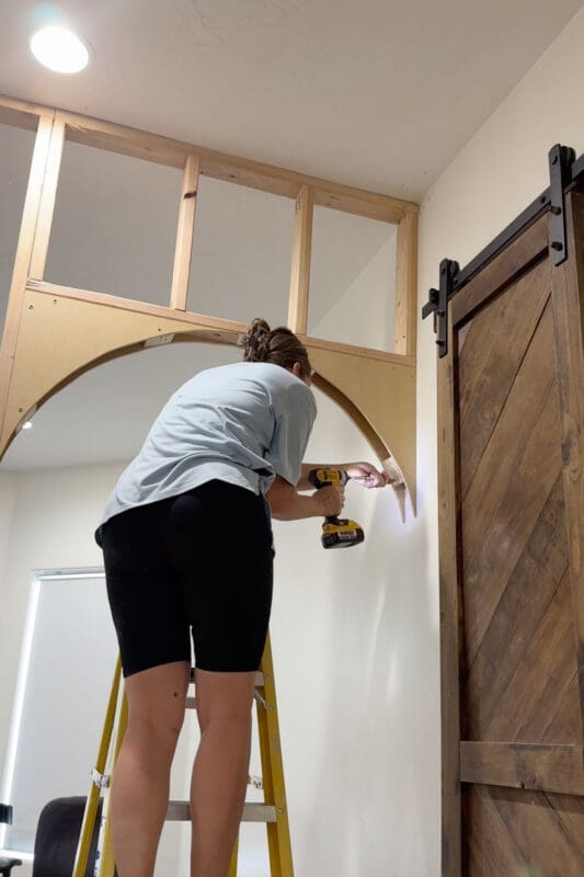 Crystel holding an MDF arch corner piece against the framing under the new 2x4 frame and screwing it into place