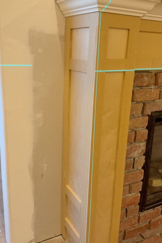 Close-up of MDF box molding panels on the side and front of the fireplace column, with green laser level lines marking where the trim pieces line up