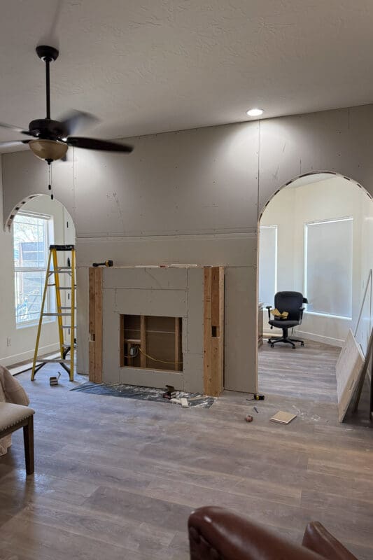 Divider wall covered in fresh drywall with an arched doorway on each side and a framed fireplace bump-out in the center, with an open recess where the electric fireplace insert will go