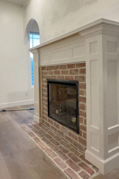 Completed electric fireplace with a painted white mantel and box molding columns framing the red brick surround and hearth, before the wall above was finished and decorated