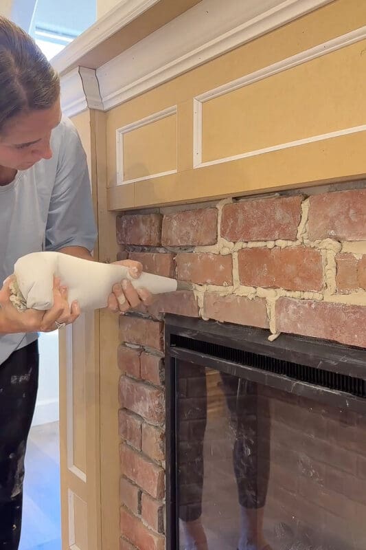 Crystel using her finger to press and smooth the piped mortar into the joints between the bricks above the electric fireplace insert