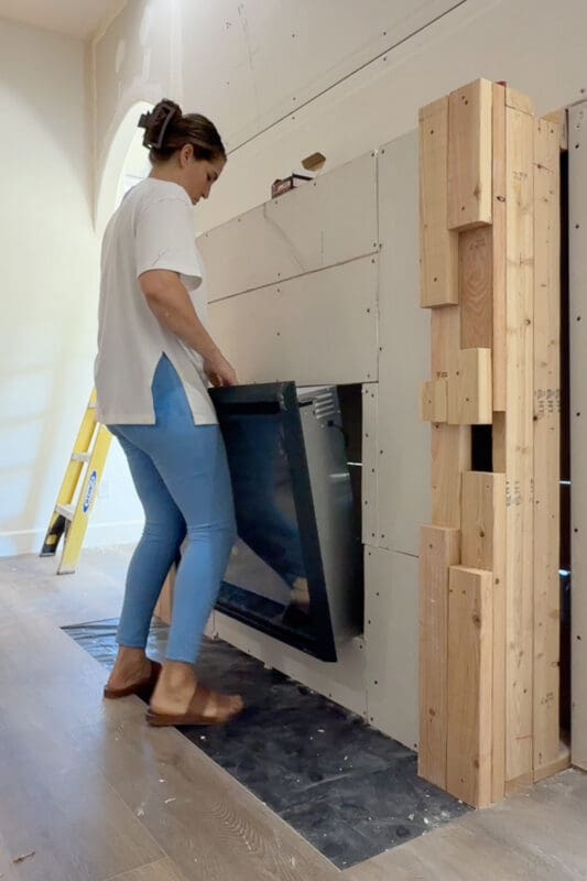 Crystel lifting the electric fireplace insert and sliding it into the recessed opening in the framed fireplace surround