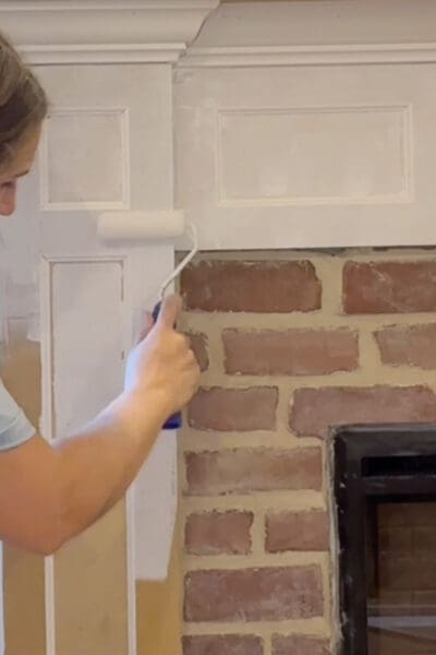 Crystel using a small roller to paint the box molding trim on the fireplace surround white, with the finished brick and mortar joints beside it