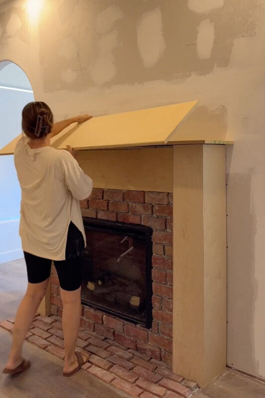 Crystel lifting a sheet of plywood into place on top of the fireplace surround to form the mantel shelf